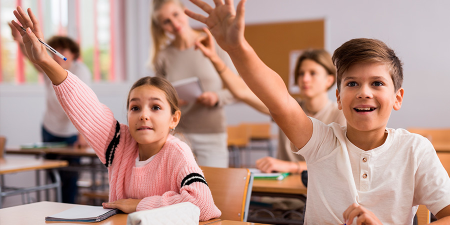 alunos em sala com as mãos levantadas 